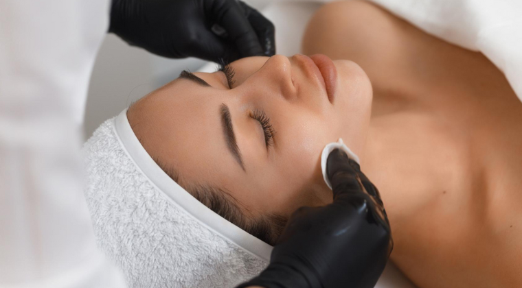 Woman receiving a chemical peel treatment by an esthetician wearing black gloves